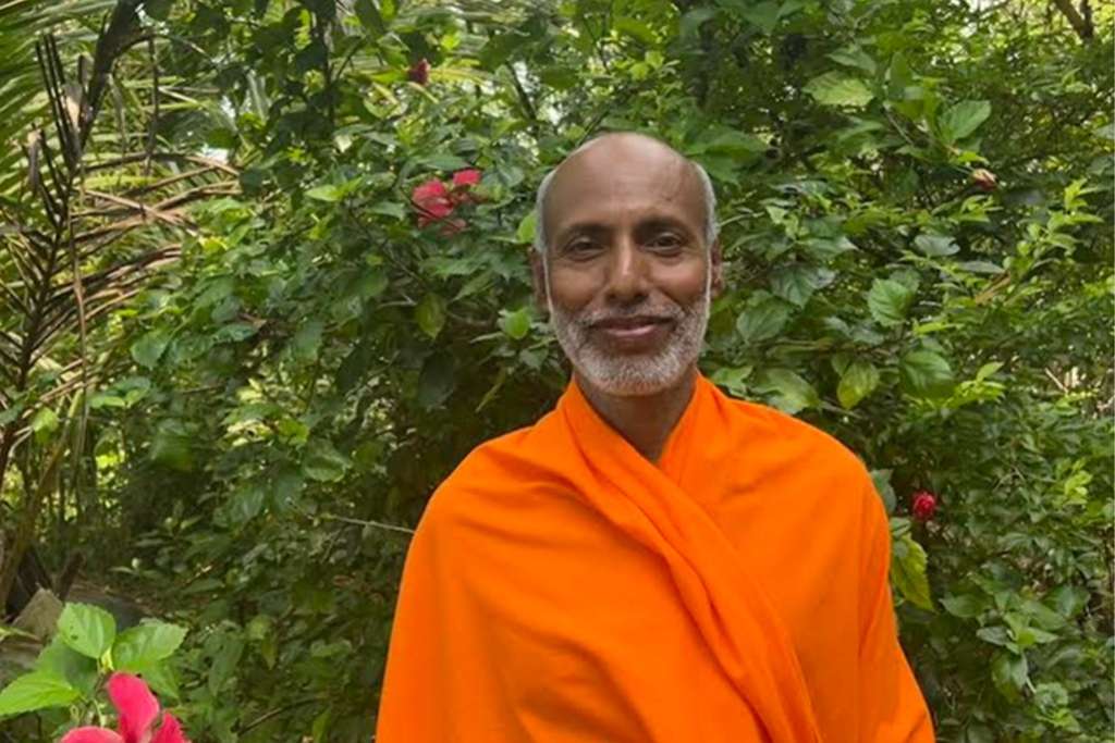 A serene man in an orange robe standing amidst lush greenery, radiating peace and wisdom.