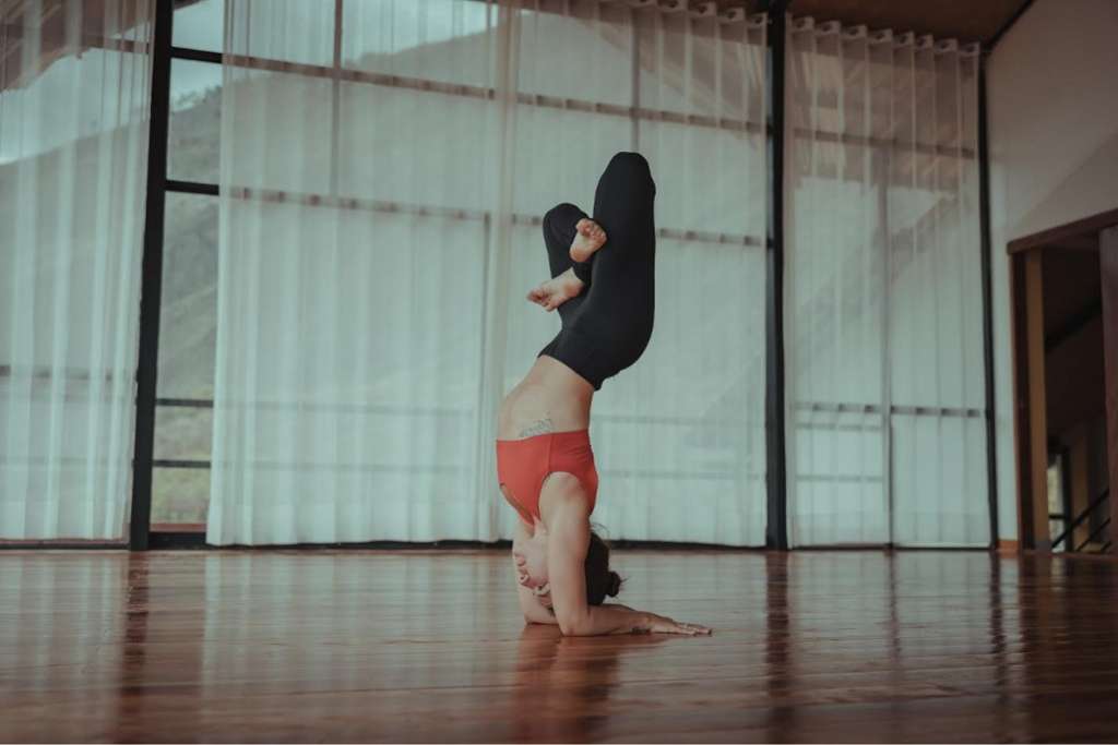 A woman performing a forearm stand yoga pose in a studio with soft natural lighting.