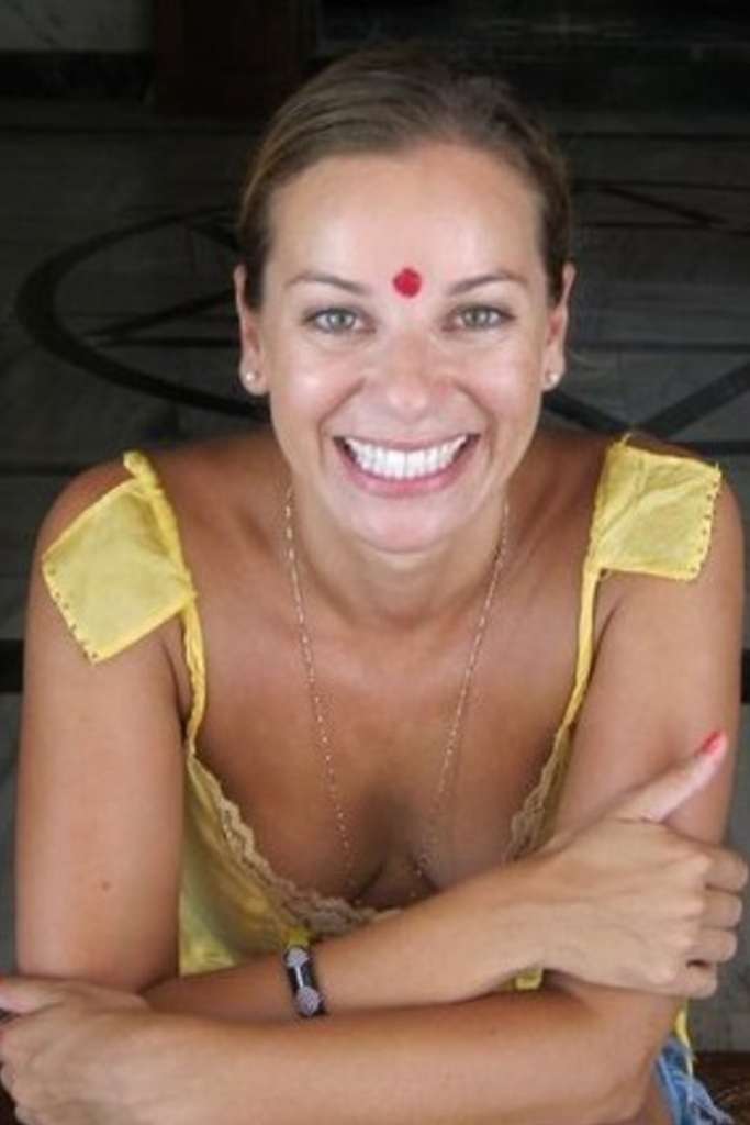 A cheerful woman with a radiant smile, wearing a yellow top and a red bindi on her forehead.