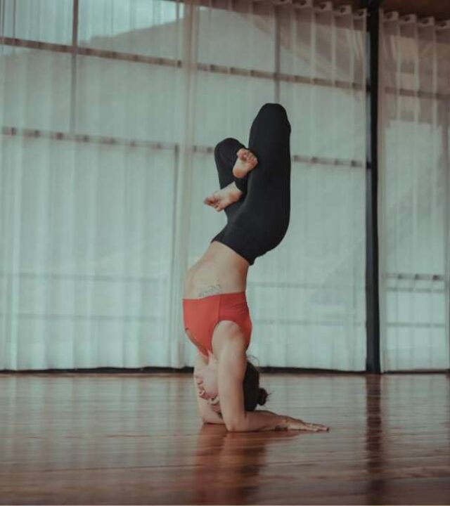 A woman performing a forearm stand yoga pose in a studio with soft natural lighting.